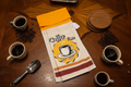 The Family Creation, LLC non-slip stove towel featuring a Coffee Time design with gold accents on a wooden table.